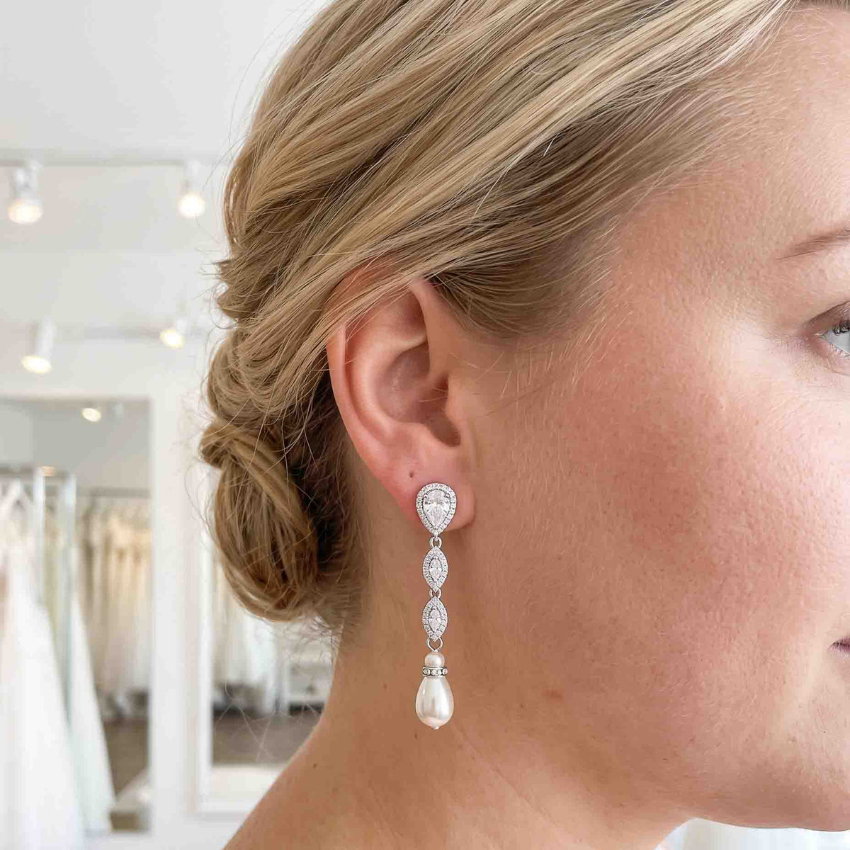 Close-up of an Abby silver crystal and teardrop pearl earring worn with a low bridal bun by a bride