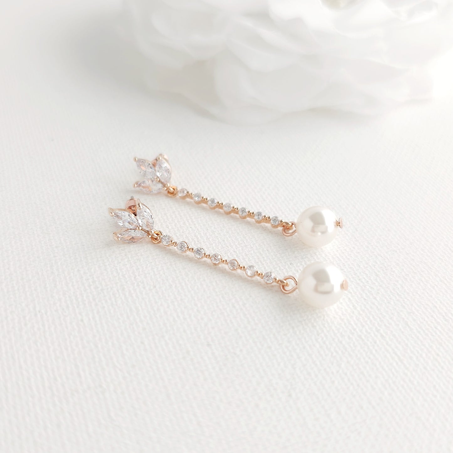 Pair of delicate earrings with rose gold and pearl details on a white fabric background