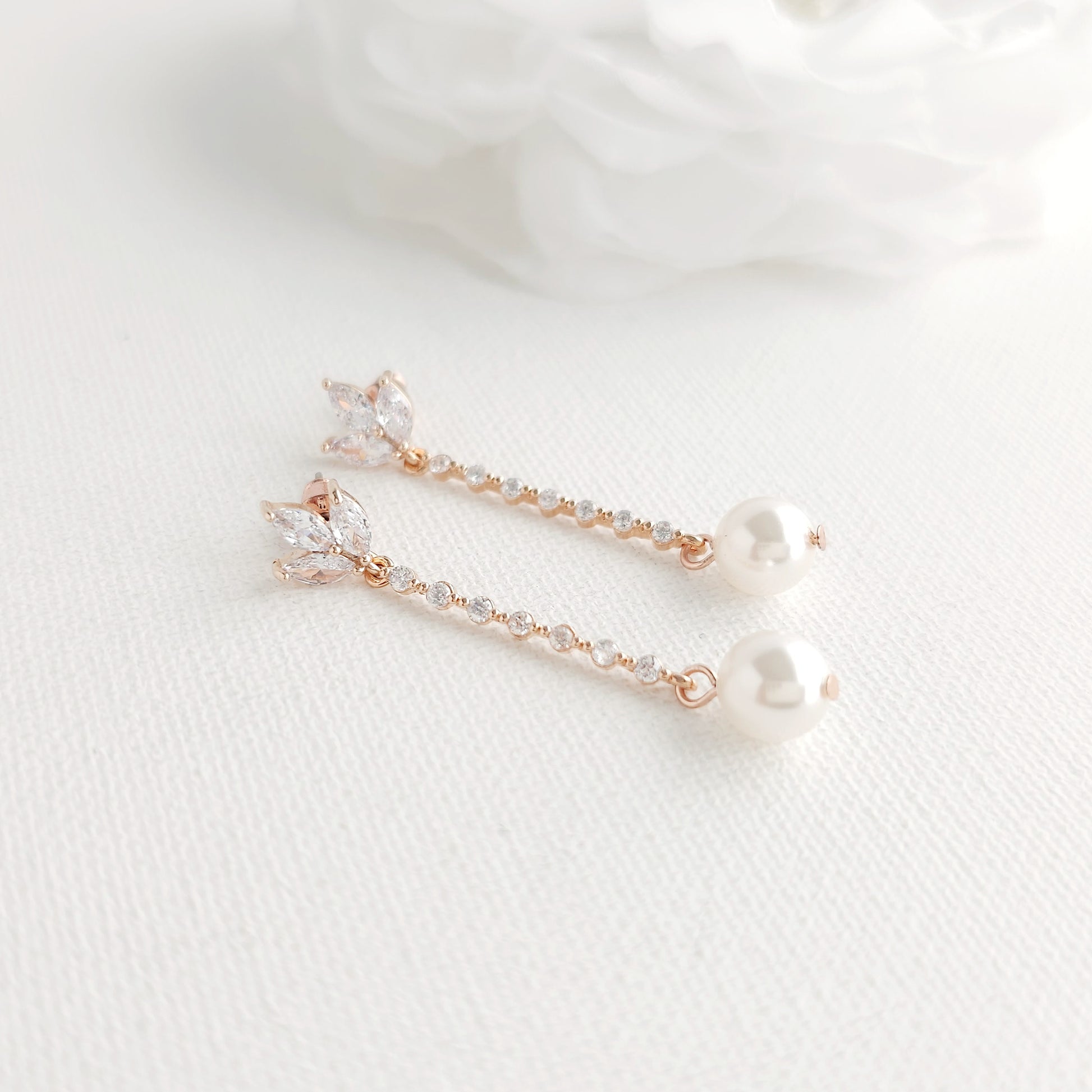 Pair of delicate earrings with rose gold and pearl details on a white fabric background