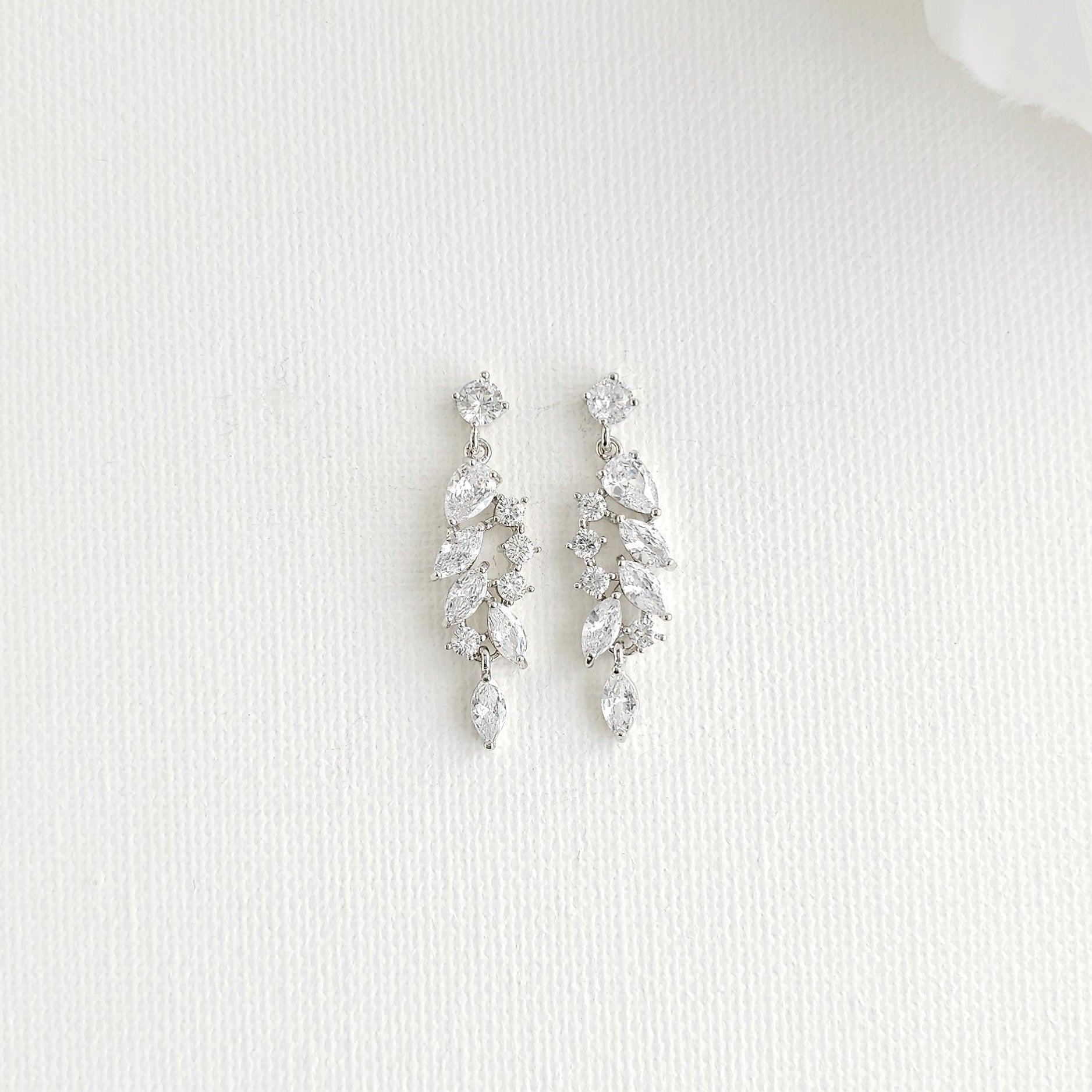 A pair of silver-toned drop earrings with marquise clear stones arranged in a leaf-like cluster, displayed on a textured white surface.